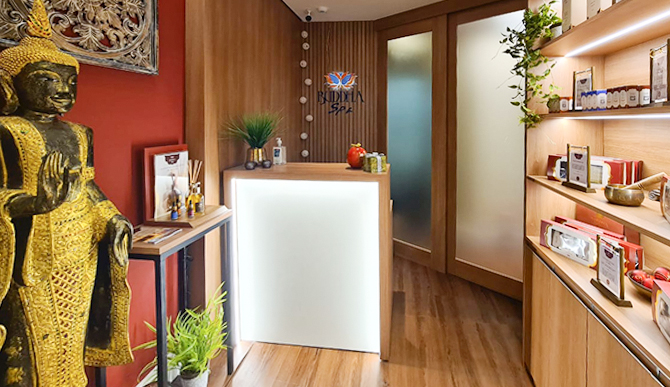 Recepção do Buddha Spa Granja Viana. Uma imagem grande do Buddha ao lado esquerdo da foto. Uma prateleira com produtos Buddha Spa expostos e um balcão ao fundo.